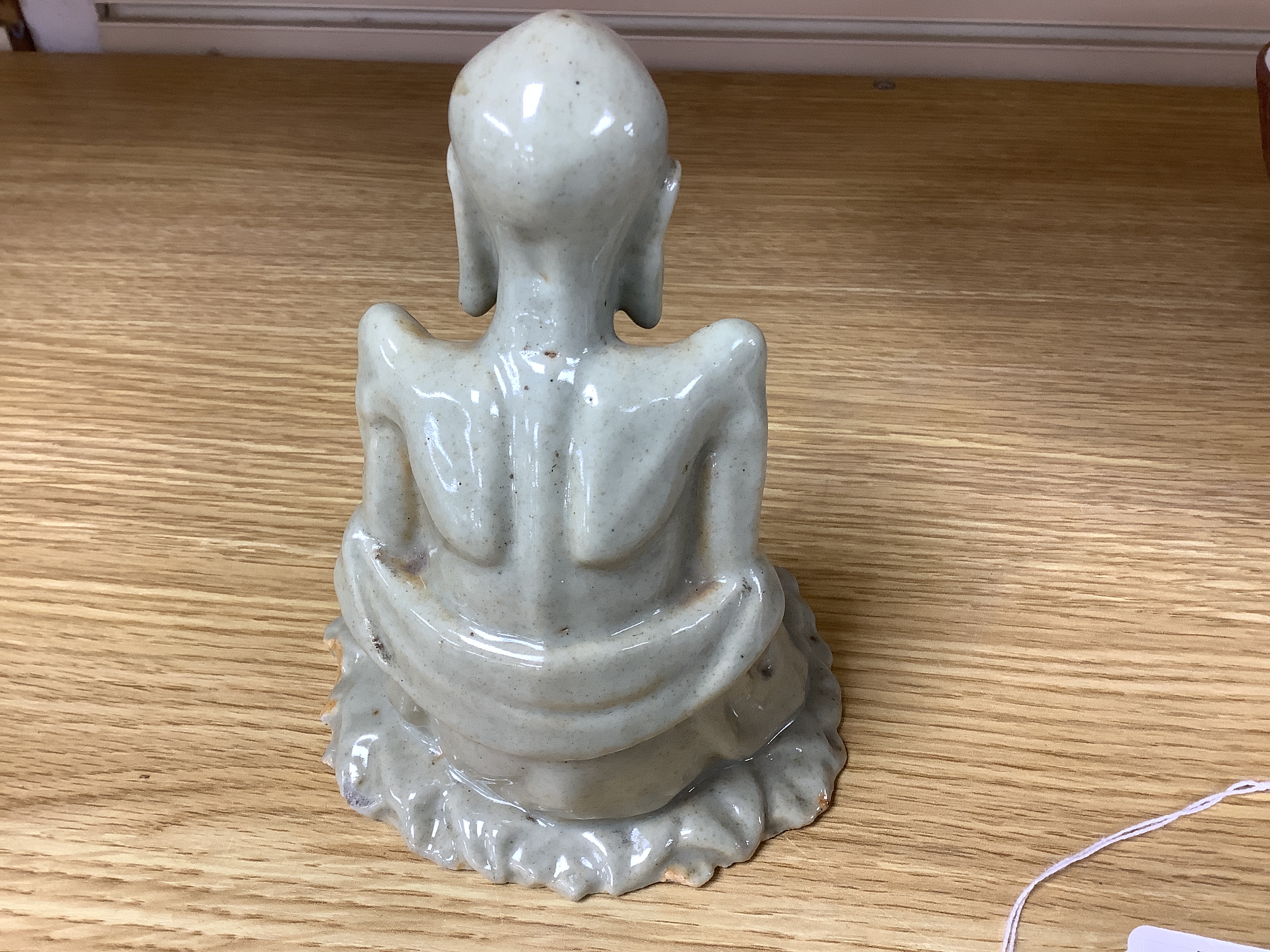 A Chinese celadon glazed figure of Laozi, 18th / 19th century, cross-legged and seated on leaves, 15cm high